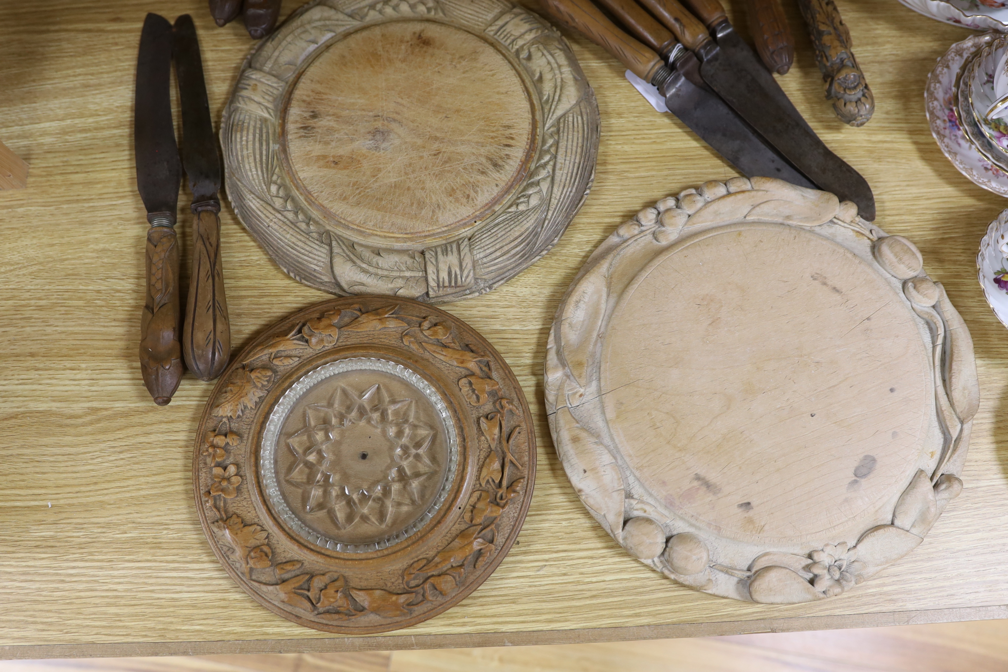 Three carved wood breadboards, a butter dish and a collection of knives with carved handles, largest 29cm in diameter